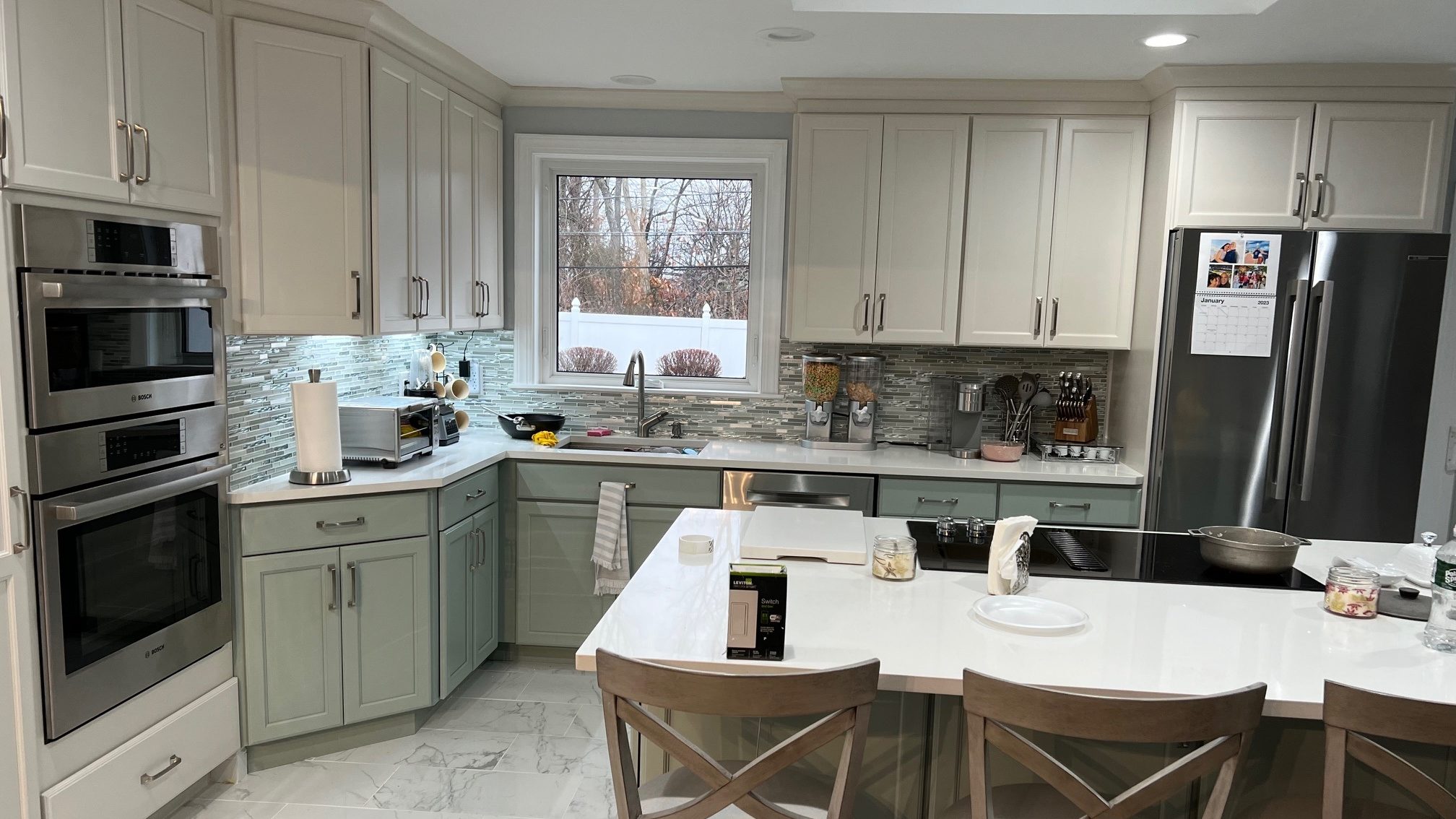 Remodeled kitchen with sage cabinets, a white island and double wall ovens